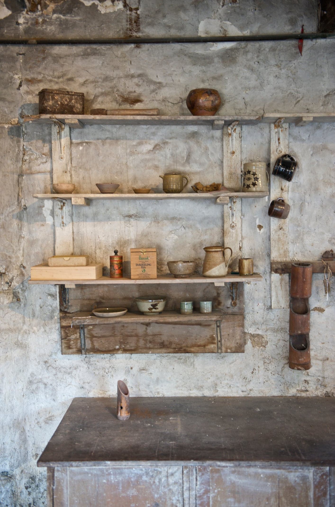 Mur chaulé d'un atelier de potier : étagères en bois chargées de bols, de pots et d'outils